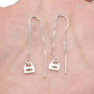 May include: A pair of silver lock charm dangle earrings. The earrings are made of a delicate chain with a small lock charm at the bottom.