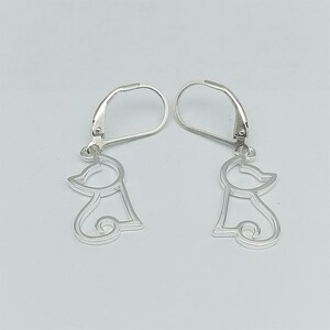 May include: A pair of silver dangle earrings featuring a simple outline of a cat. The earrings have a leverback closure.