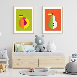 May include: Two framed illustrations of fruit, a peach and a pear, with the words "Peach | Prunus persica" and "Pear | Pyrus communis" printed below each fruit. The illustrations are hanging on a white wall above a wooden daybed with a white mattress and a light blue and white striped pillow. There are several stuffed animals on the daybed, including a gray teddy bear, a white bunny, and a gray whale.