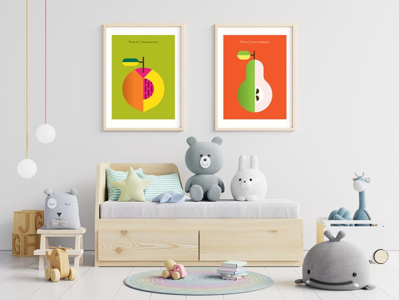May include: Two framed illustrations of fruit, a peach and a pear, with the words "Peach | Prunus persica" and "Pear | Pyrus communis" printed below each fruit. The illustrations are hanging on a white wall above a wooden daybed with a white mattress and a light blue and white striped pillow. There are several stuffed animals on the daybed, including a gray teddy bear, a white bunny, and a gray whale.