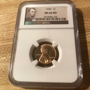 May include: A 1944 1C Lincoln penny graded MS 66 RD by NGC in a plastic slab. The coin is in a clear plastic holder with a white label that reads "1944 1C MS 66 RD 3919085-165 NGC".