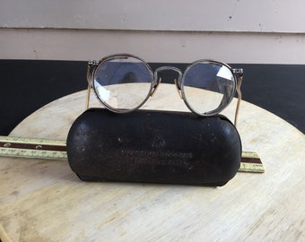 May include: Vintage round metal frame glasses with clear lenses in a black leather case with the text "Vogue Products Made in USA".