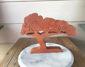 May include: A wooden tree puzzle with a brown finish. The tree has a thick trunk and branches with leaves that are shaped like puzzle pieces. The tree is sitting on a white marble base.