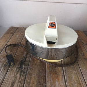 May include: A white and chrome electric ice shaver with a handle and a black power cord. The shaver has a yellow base and the brand name "Sunbeam" is printed on the handle.