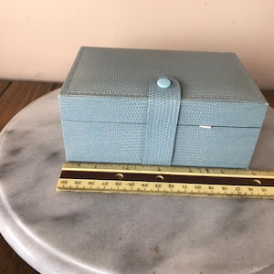 May include: A light blue rectangular box with a textured surface and a light blue button closure. The box is sitting on a marble surface.