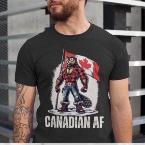 May include: Black t-shirt featuring a cartoon beaver in sunglasses and a red plaid shirt, holding a Canadian flag. The text "CANADIAN AF" is printed below the graphic.