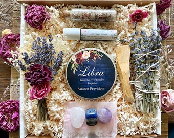 May include: A gift box filled with items for a Libra zodiac sign. The box contains a small wooden spoon, a bundle of dried lavender, a small bottle of bath salts, a small round tin with the words "Libra, Graceful - Friendly - Popular,  Saracen Provisions" on it, and three crystals: a pink rose quartz, a blue lapis lazuli, and a purple amethyst.