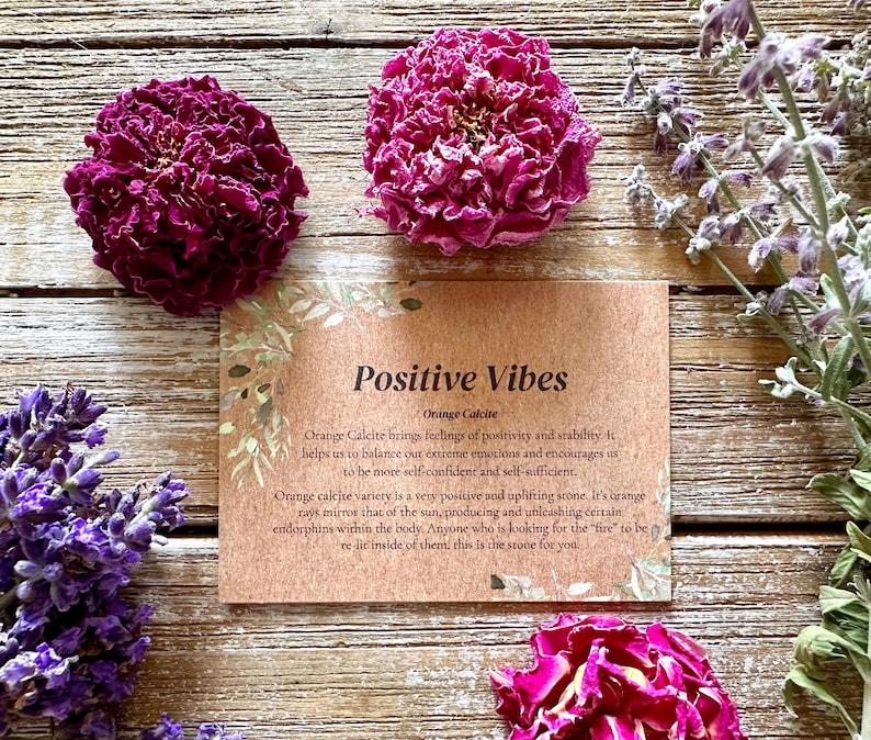 Pu&ograve; includere: Un biglietto marrone con il testo "Positive Vibes" e "Orange Calcite" su di esso. Il biglietto &egrave; circondato da fiori secchi, tra cui lavanda e rose.