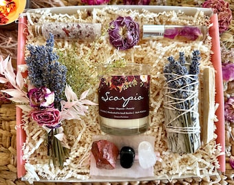 May include: A gift box filled with items for the zodiac sign Scorpio. The box contains a candle, a sage smudge stick, a bath salt, a crystal set, and dried flowers. The candle is labeled "Scorpio" and has a floral design. The sage smudge stick is tied with twine and has dried lavender flowers. The bath salt is in a small glass bottle with dried rose petals. The crystal set includes a red, black, and white crystal. The dried flowers are a mix of lavender and roses.