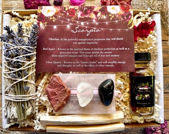 May include: A gift box set for Scorpio zodiac sign. The box contains a white sage smudge stick, a red agate crystal, a clear quartz crystal, a black obsidian crystal, and a bottle of bath and body oil. The box is decorated with a card that says "Scorpio" and has information about the crystals and oil.