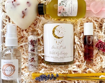 May include: A gift box filled with self-care items, including a white sage smudge spray, a candle with the text "Don't F*ck With My Energy", a heart-shaped bath bomb, a bottle of lavender oil, a small jar of bath salts, a roll-on bottle of essential oil, and a yellow candle stick.