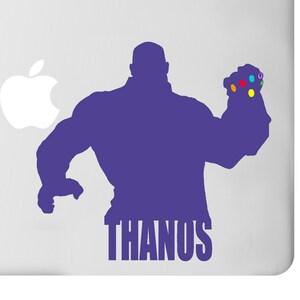May include: A purple silhouette of Thanos with the Infinity Gauntlet on a white laptop. The gauntlet features colorful gems. The word "THANOS" is printed in a bold font below the character.