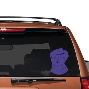 May include: Purple vinyl car decal featuring a stylized gauntlet design. The decal is affixed to the rear window of an orange SUV. The gauntlet design has a cartoonish appearance.