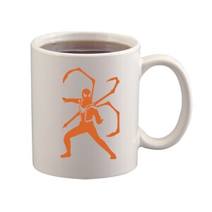 May include: White ceramic mug with a handle, filled with a dark liquid. The mug features an orange silhouette of a superhero with multiple mechanical arms. The design is centered on the mug's surface.