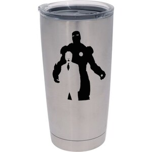 Puede incluir: Un vaso de acero inoxidable con tapa transparente. El vaso presenta una silueta negra de un hombre con traje frente a una silueta de Iron Man. El vaso est&aacute; dise&ntilde;ado para mantener las bebidas fr&iacute;as o calientes.