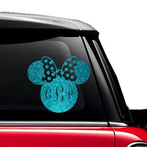 May include: A teal glitter vinyl decal in the shape of Minnie Mouse's head, with a black polka dot bow and custom initials. The decal is applied to a car window.