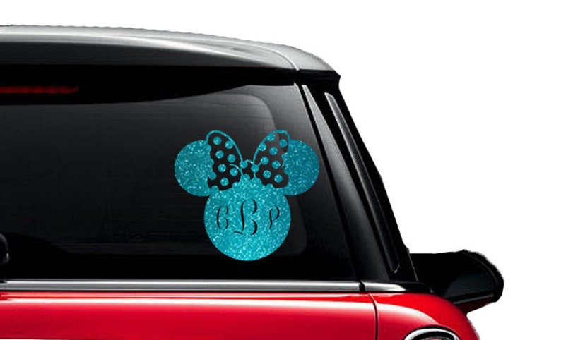 May include: A teal glitter vinyl decal in the shape of Minnie Mouse's head, with a black polka dot bow and custom initials. The decal is applied to a car window.
