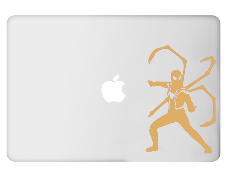 May include: A white laptop with a gold Spider-Man design. The design features a stylized Spider-Man figure with multiple mechanical arms extending from his back. The Apple logo is visible on the left side of the laptop.