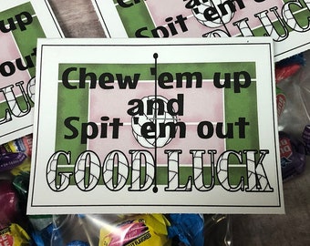 Pode incluir: Um cartão branco com listras verdes e rosa e o texto "Chew 'em up and Spit 'em out GOOD LUCK" em letras pretas.