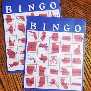 Pode incluir: Um cartão de bingo azul e branco com a palavra "BINGO" no topo. O cartão é dividido em uma grade de 5x5 com cada quadrado contendo o contorno de um estado dos EUA. O quadrado central diz "FREE SPACE".