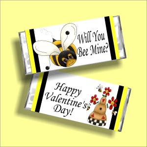 May include: Two white chocolate bar wrappers with black and yellow borders. The top wrapper features a cartoon bee with the text "Will You Bee Mine?" The bottom wrapper features a beehive with flowers and the text "Happy Valentine's Day!"