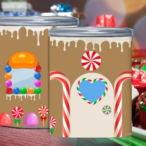 Może przedstawiać: Dwa brązowe, cylindryczne pojemniki ze srebrnymi pokrywkami, ozdobione jako domki z piernika. Jeden ma okno z cukierków i kolorowych słodyczy, drugi ma drzwi w kształcie serca i akcenty lasek cukrowych.