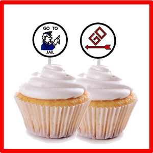 Peut inclure: Deux cupcakes avec du gla&ccedil;age blanc et un topper sur le th&egrave;me du jeu de soci&eacute;t&eacute; Monopoly. Un topper dit "Go to Jail" avec un homme Monopoly pointant vers le texte. L'autre topper a une fl&egrave;che rouge pointant vers un symbole "GO" rouge.