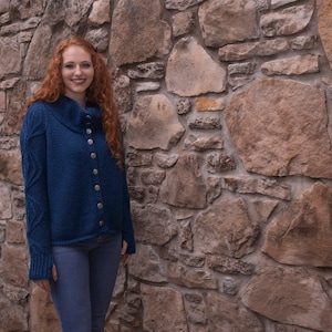 以下が含まれることがあります： ハイネックとボタン留めの青いニットカーディガン。カーディガンは柔らかく、質感のある糸でできており、ゆったりとしたフィット感です。