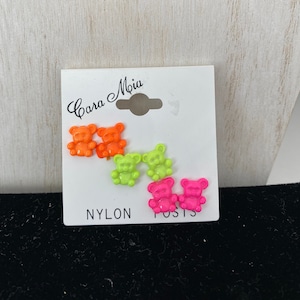 May include: A set of six neon-colored bear stud earrings. The earrings are pink, green, and orange. The card reads "Cara Mia" and "Nylon Posts".