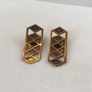 May include: A pair of gold-toned earrings with a geometric design. The earrings are made of metal and have a brown enamel finish. The design features a series of interlocking triangles.