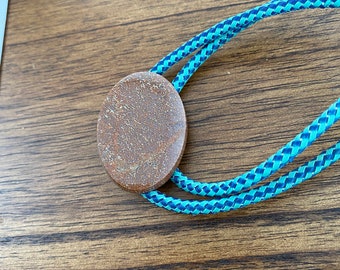 May include: A brown wooden bolo tie with a blue and turquoise braided cord.