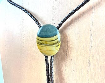 May include: A brown leather bolo tie with a round, multi-colored stone pendant. The stone has a yellow, blue, and brown pattern.