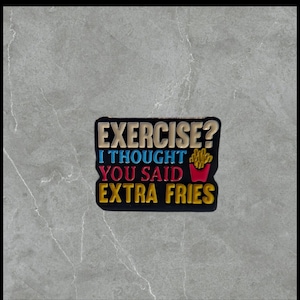May include: A black, rectangular pin with the text "EXERCISE? I THOUGHT YOU SAID EXTRA FRIES" in gold, blue, red, and yellow. The pin features a graphic of french fries in a red container.