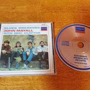 May include: A CD case with a photo of four men on the front. The text on the front reads "Blues Breakers John Mayall with Eric Clapton". The CD case is black with a silver spine.