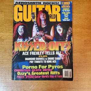 May include: A vintage Guitar World magazine cover featuring Aerosmith and the band Kiss. The cover includes text such as "Kissed Off!" and "Ace Frehley Tells All." The magazine is on a wooden surface.