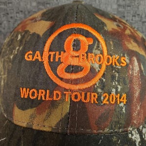 Peut inclure: Une casquette de baseball camouflage avec un logo brod&eacute; orange qui dit "Garth Brooks World Tour 2014".