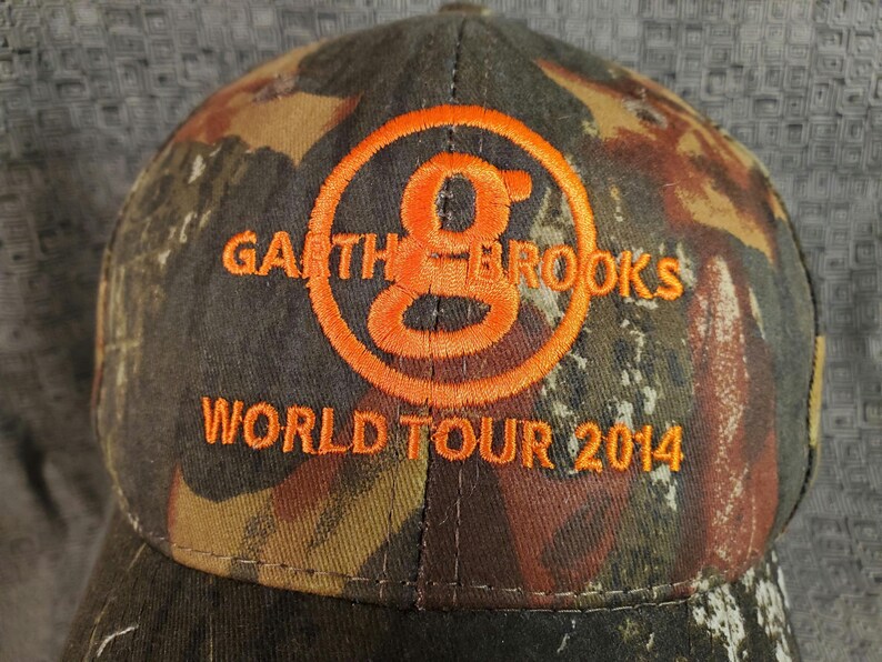 Peut inclure: Une casquette de baseball camouflage avec un logo brod&eacute; orange qui dit "Garth Brooks World Tour 2014".