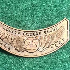 May include: A bronze Harley Owners Group patch with wings and the text "Harley Owners Group" and the years "1983" and "2008" on either side of a circle with the number "25" inside.