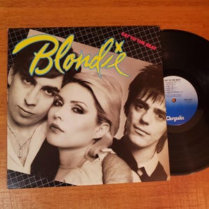 May include: A vinyl record album cover for Blondie's "Eat to the Beat" album. The cover features a photo of the band members with the band's name in yellow and blue. The record is black.