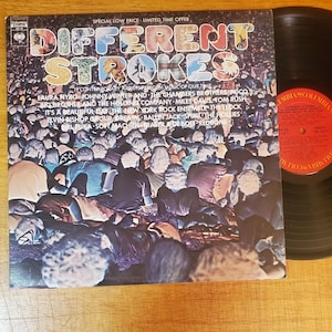 May include: A vinyl record album titled Different Strokes featuring a crowd scene on the cover. The text lists 19 contemporary artists including Laura Nyro, Johnny Winter, and The Chambers Brothers. A black vinyl record with a red Columbia label is visible.