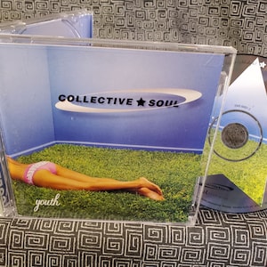 May include: A CD case with a blue and white background featuring a woman lying on green grass. The text "COLLECTIVE SOUL" and "youth" are visible on the case.