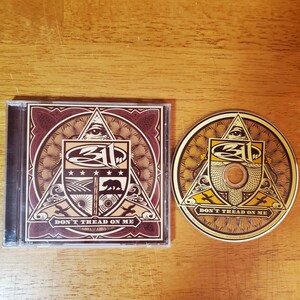 May include: A CD case and disc featuring a brown and gold design with the text "DON'T TREAD ON ME". The artwork includes an eye within a triangle, stars, a bear, and other symbols. The CD case is rectangular and the disc is circular.