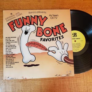 May include: A vintage vinyl record titled "Funny Bone Favorites" by Ronco, featuring cartoon illustrations of a bone and gloved hand. The album cover includes a list of song titles and the text "As Seen On TV."