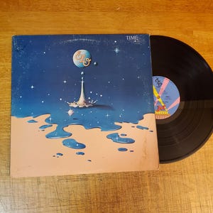 May include: A vinyl record album titled Time by ELO, featuring a square cardboard sleeve with a blue space-themed illustration of a planet and liquid splash, alongside a black circular vinyl disc with a blue and pink center label.