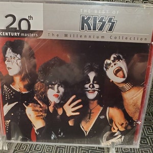 May include: A CD case featuring the band KISS. The case is silver with black text that reads "The Best of KISS" and "The Millennium Collection". The band members are pictured on the front of the case, wearing their signature makeup.
