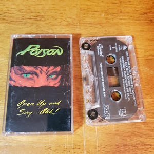 May include: A vintage cassette tape of the album "Open Up and Say... Ahh!" by Poison. The album cover features the band's logo in green and an illustration of eyes. The cassette is clear with the tracklist visible.