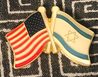May include: A gold pin with two crossed flags. The flag on the left is the American flag with red and white stripes and blue stars. The flag on the right is the Israeli flag with blue and white stripes and a six-pointed star.