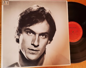 May include: A black and white album cover featuring a portrait of a man with dark hair. The album cover has the letters "JT" in the upper left corner. A black vinyl record is visible to the right. The record label is red.