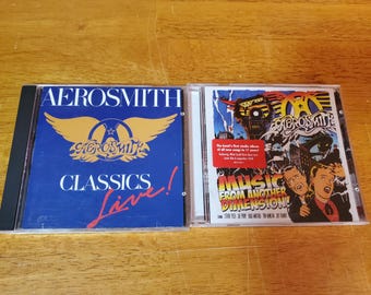 May include: Two compact discs, one blue with the text "Aerosmith Classics Live!" and the other with a colorful illustration of the band and the text "Music From Another Dimension!"