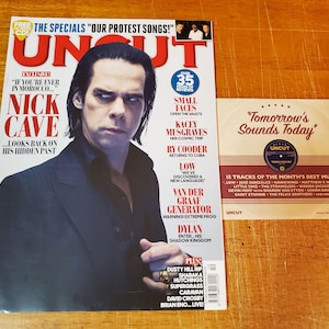 May include: A magazine cover featuring Nick Cave with the word "UNCUT" in large red letters. The cover also includes text about music and reviews. A small CD with the text "Tomorrow's Sounds Today" is next to the magazine.